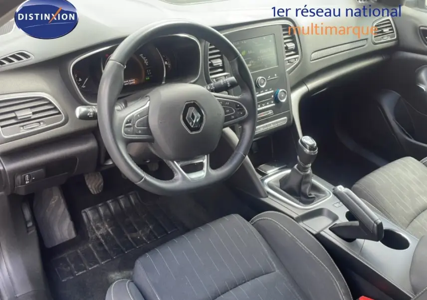 Intérieur de Renault Mégane 2021 vu côté conducteur, volant cuir, tableau de bord avec écran tactile et levier de vitesse manuel.