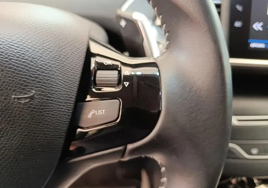 Gros plan sur le volant cuir noir de la Peugeot 308 2020 avec commandes multifonctions et écran tactile en arrière-plan.