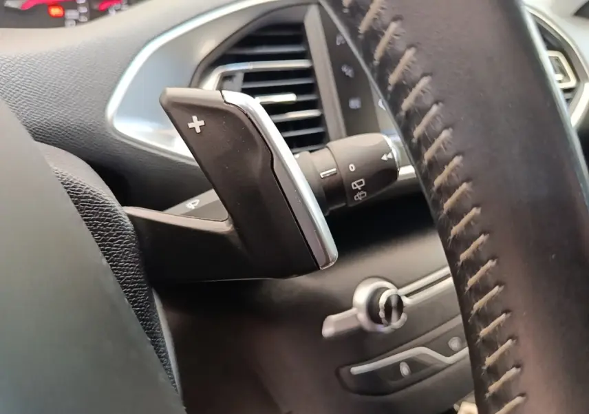 Gros plan sur la palette de changement de vitesse droite et partie du volant cuir noir du Peugeot 308 blanc, intérieur.