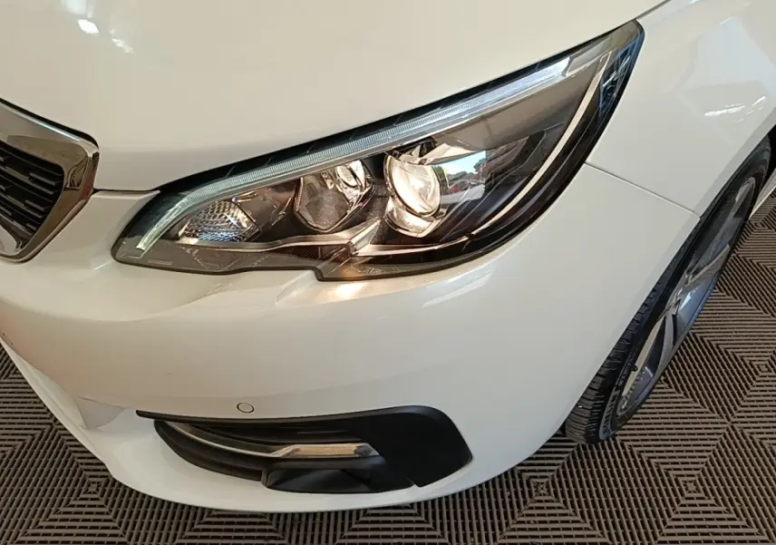 Gros plan sur le phare avant droit blanc d’une Peugeot 308 avec calandre chromée et antibrouillard intégré.