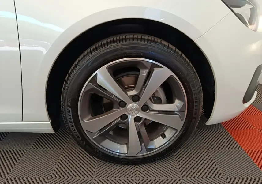 Gros plan sur la roue avant droite d'une Peugeot 308 blanche, jante alliage gris foncé, pneu Michelin visible.
