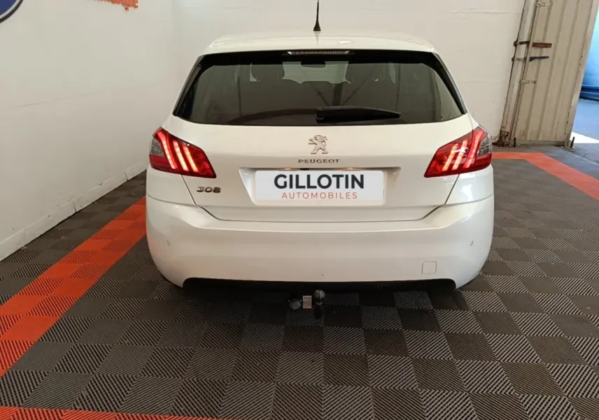 Vue arrière d'une Peugeot 308 blanche avec feux arrière allumés et attelage visible en intérieur showroom.