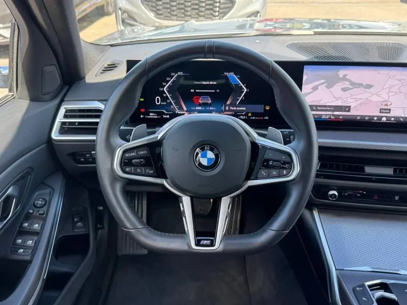 Vue intérieure centrée sur le volant M Sport de la BMW Série 3 320dA xDrive 2025 avec tableau de bord numérique et écran tactile.