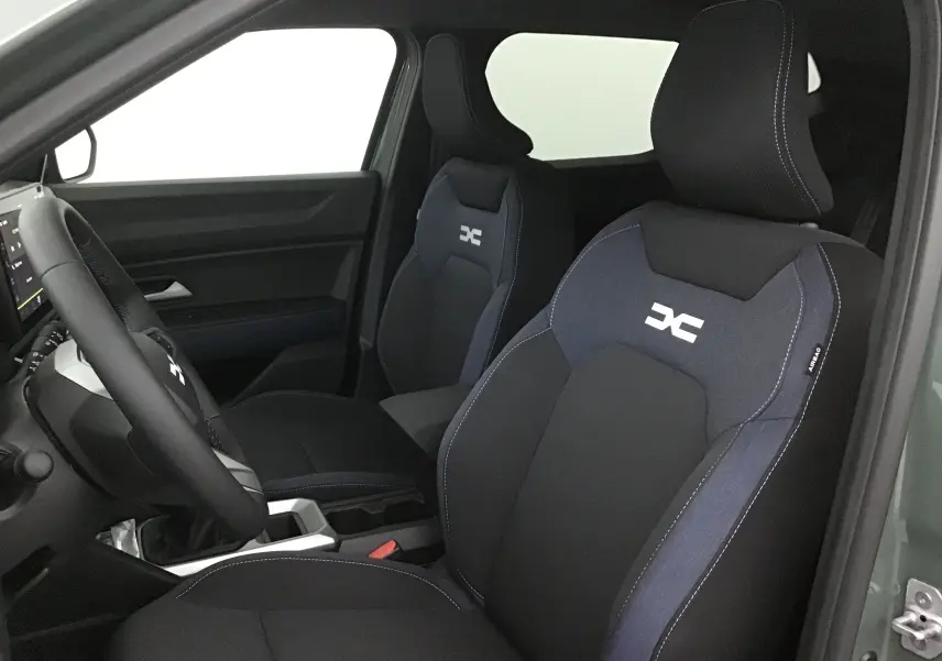 Vue intérieure côté conducteur du Dacia Duster 2025 avec sièges noirs et logo blanc sur appuie-tête, ambiance sobre et moderne.