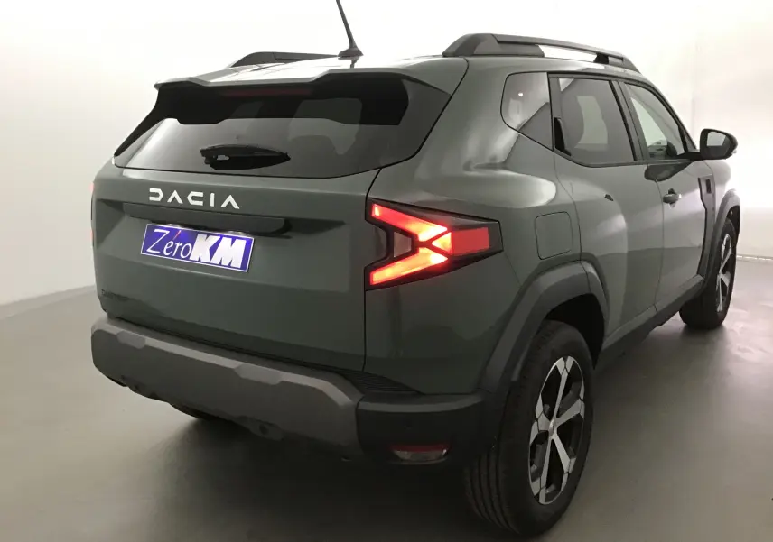 Vue 3/4 arrière droite du Dacia Duster 2025 kaki lichen avec feux arrière allumés et jantes alliage noires.