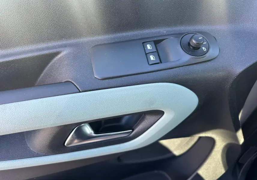 Gros plan sur la commande de lève-vitres et le bouton de réglage des rétroviseurs côté gauche intérieur d’un Citroën Berlingo gris clair.