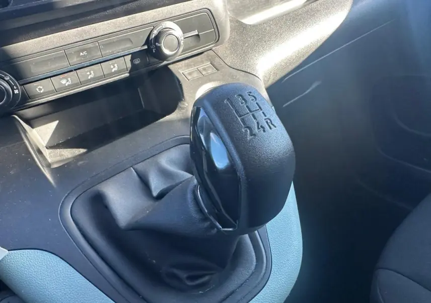 Gros plan sur le levier de vitesses manuel noir du Citroën Berlingo gris clair, avec commandes de climatisation en arrière-plan.