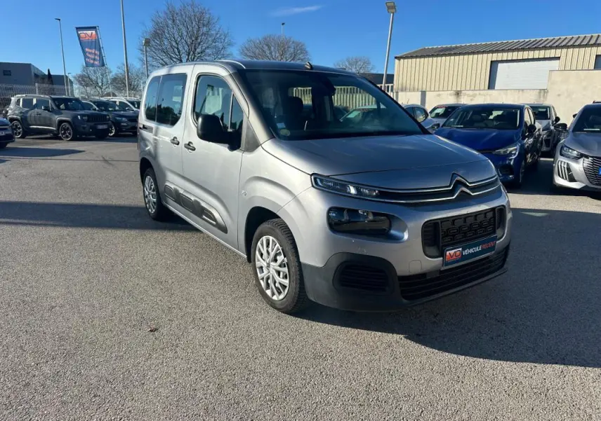 Citroën Berlingo gris clair en 3/4 avant droit, avec protections latérales noires et calandre distinctive.
