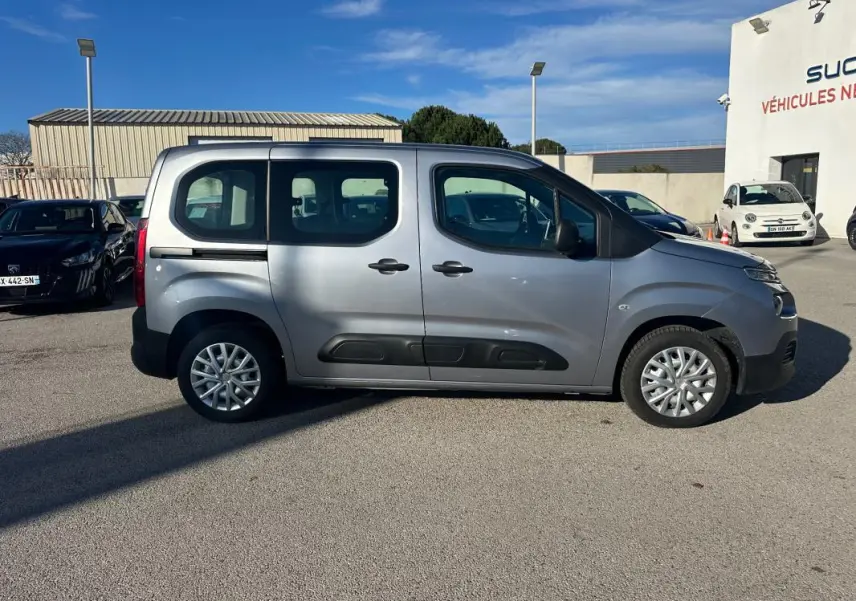 Vue de profil côté droit d'un Citroën Berlingo gris clair 2020 avec protections noires sur les portières, stationné en extérieur.