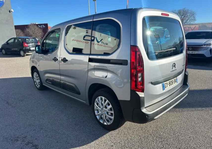 Vue 3/4 arrière droite d'un Citroën Berlingo gris clair 2020 avec vitres teintées et protections noires sur les portes.