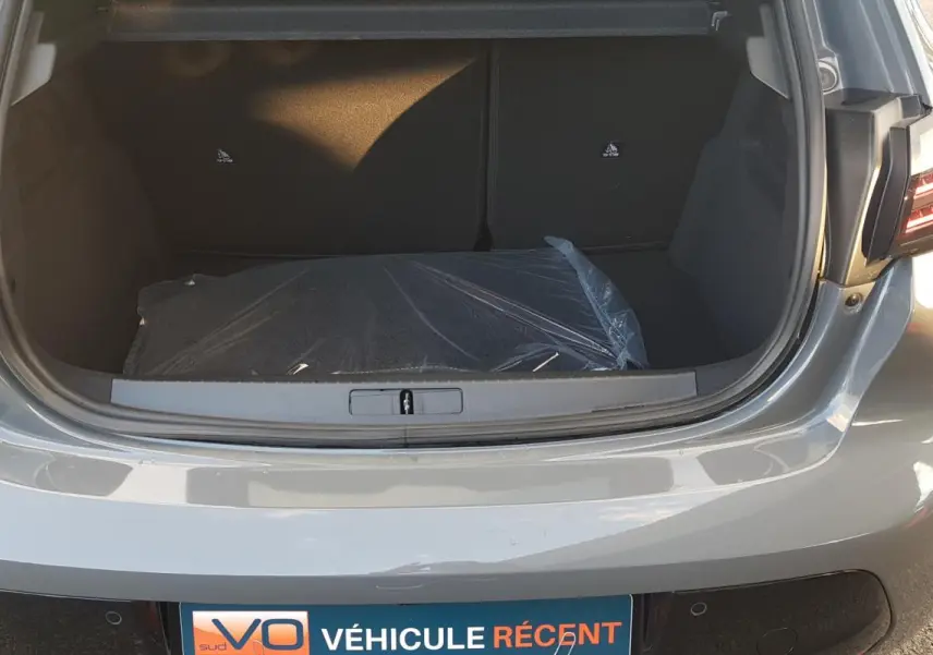 Coffre ouvert d’une Peugeot 208 Hybrid 110 e-DCS6 GT gris, vue arrière montrant l’espace de chargement vide.