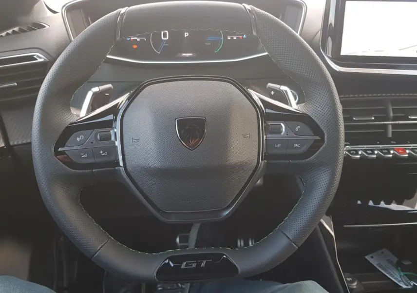 Vue intérieure centrée sur le volant GT et le cockpit numérique du Peugeot 208 Hybrid 110 e-DCS6 gris.