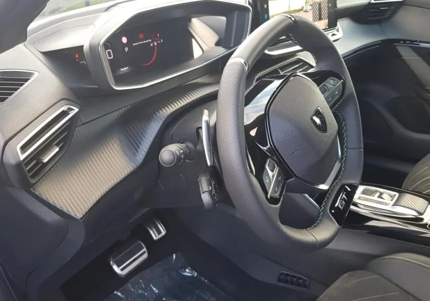 Vue intérieure côté conducteur du Peugeot 208 Hybrid gris, volant GT avec surpiqûres vertes et tableau de bord numérique.