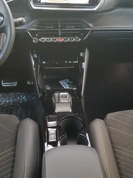 Vue intérieure centrée sur la console centrale et l'écran tactile du Peugeot 208 Hybrid 110 e-DCS6 GT, finition noire élégante.