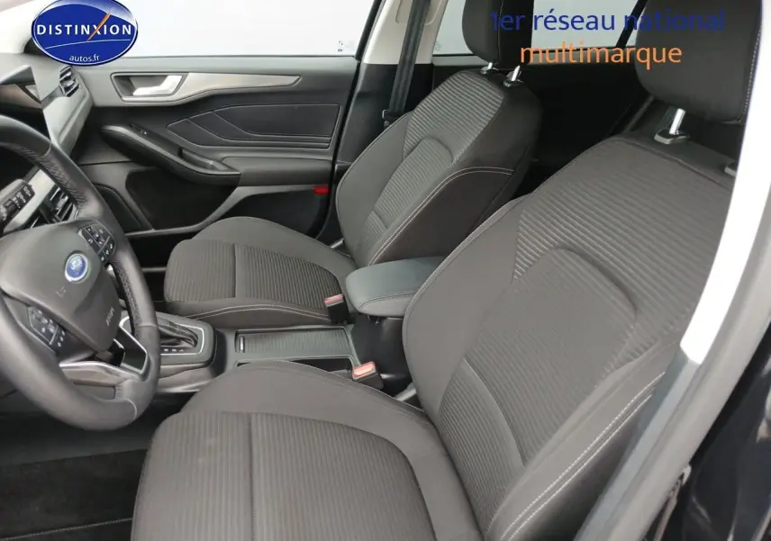 Vue intérieure côté conducteur de la Ford Focus 2024, sièges tissu noir avec accoudoir central et volant cuir multifonction.