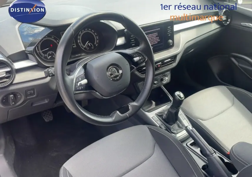 Vue intérieure centrée sur le volant cuir et la console centrale avec levier de vitesse manuelle d'une Skoda Fabia blanche.