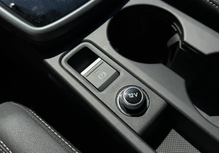 Gros plan sur la console centrale noire de l'Audi A3 Sportback 2025, avec bouton 12V et frein à main électrique.