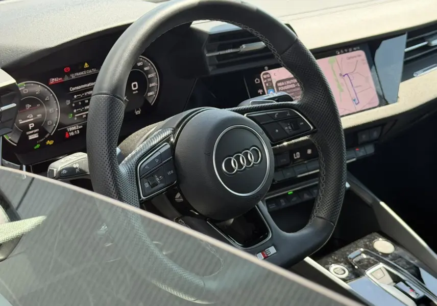 Vue rapprochée du volant sport en cuir perforé avec logo Audi et tableau de bord numérique d'une Audi A3 Sportback 2025.