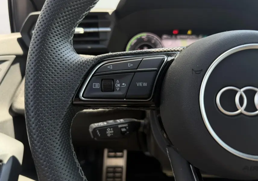 Gros plan sur le volant perforé noir de l'Audi A3 Sportback 2025, avec commandes multifonctions côté gauche.
