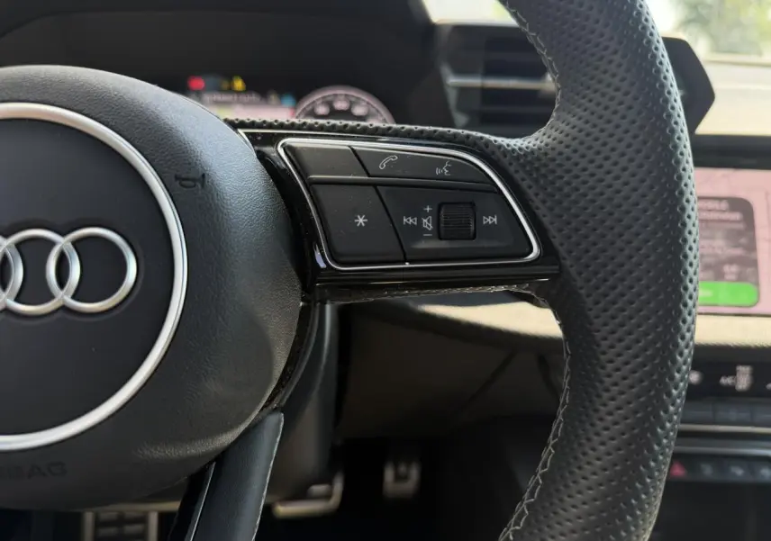 Gros plan sur le volant cuir perforé noir de l'Audi A3 Sportback 2025 avec commandes multifonctions sur le côté droit.