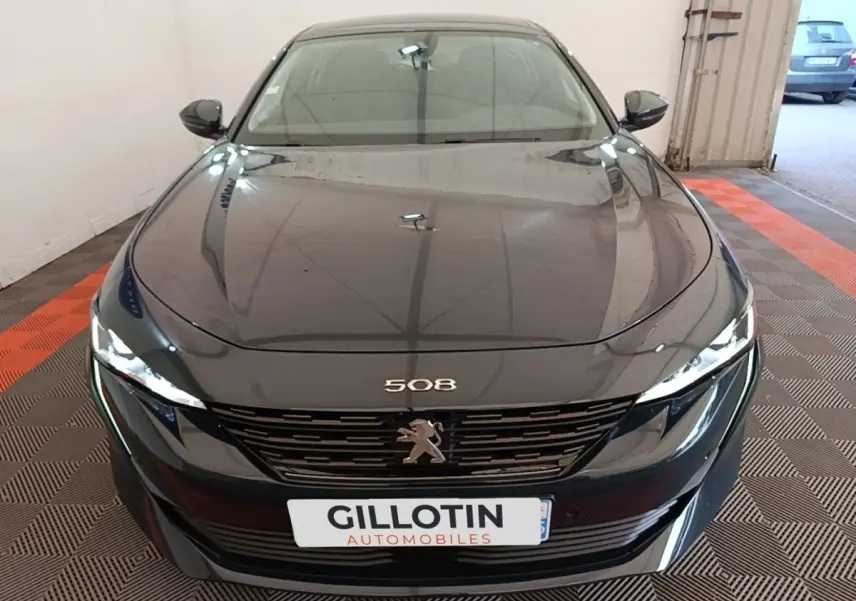 Vue frontale d'une Peugeot 508 gris foncé avec calandre noire et feux LED allumés dans un garage.