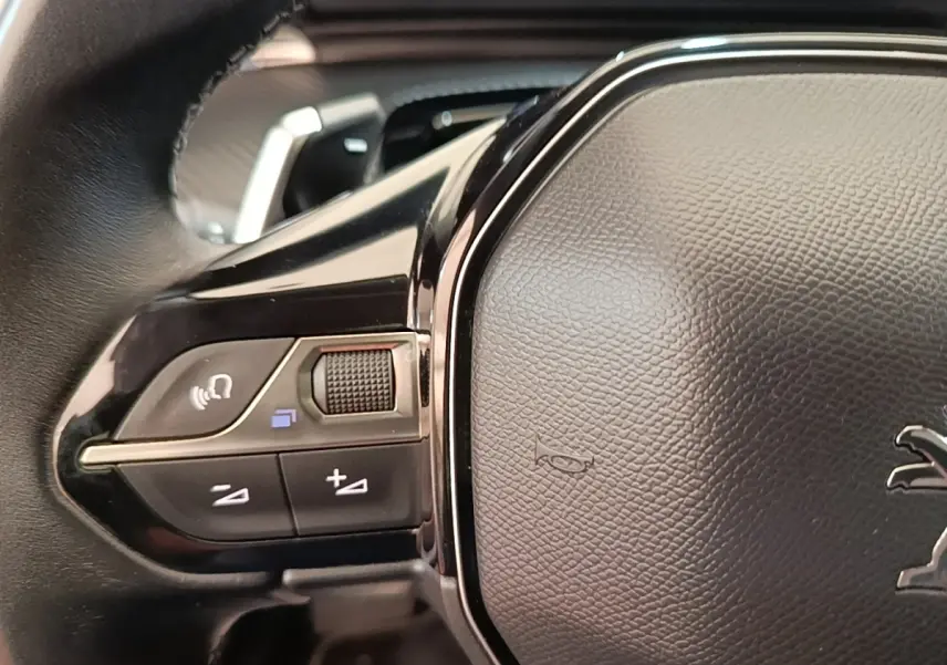 Gros plan sur le volant cuir noir de la Peugeot 508 gris foncé, avec commandes audio intégrées à gauche.