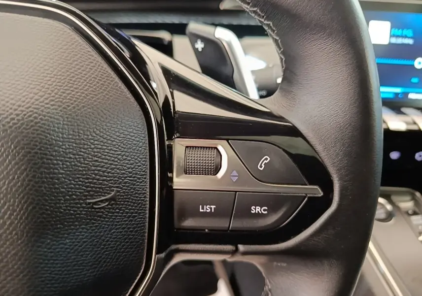 Gros plan sur le volant cuir noir de la Peugeot 508 Puretech 180, avec commandes audio et téléphone intégrées.