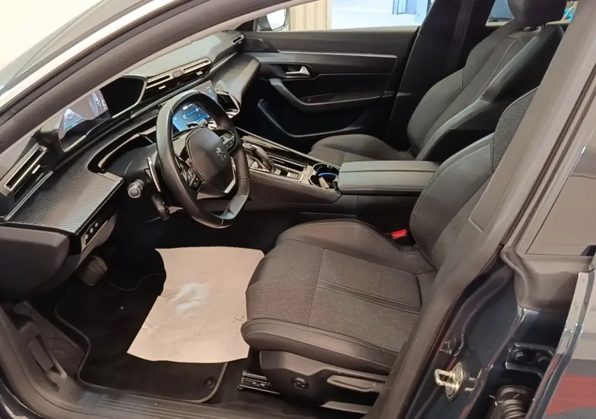 Vue intérieure côté conducteur de la Peugeot 508 gris foncé, mettant en valeur le tableau de bord numérique et les sièges en tissu et cuir.
