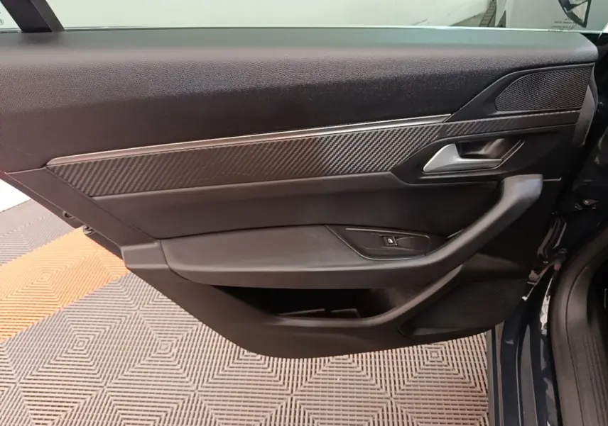 Vue intérieure côté gauche de la porte avant d’une Peugeot 508 gris foncé avec insert carbone et poignée argentée.