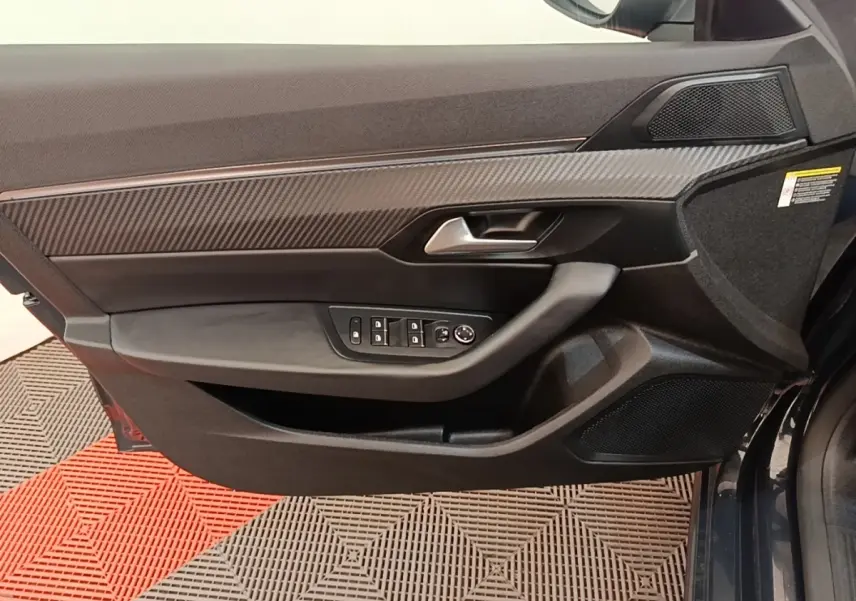 Vue rapprochée de la porte avant gauche de la Peugeot 508 gris foncé, avec garniture carbone et commandes électriques.