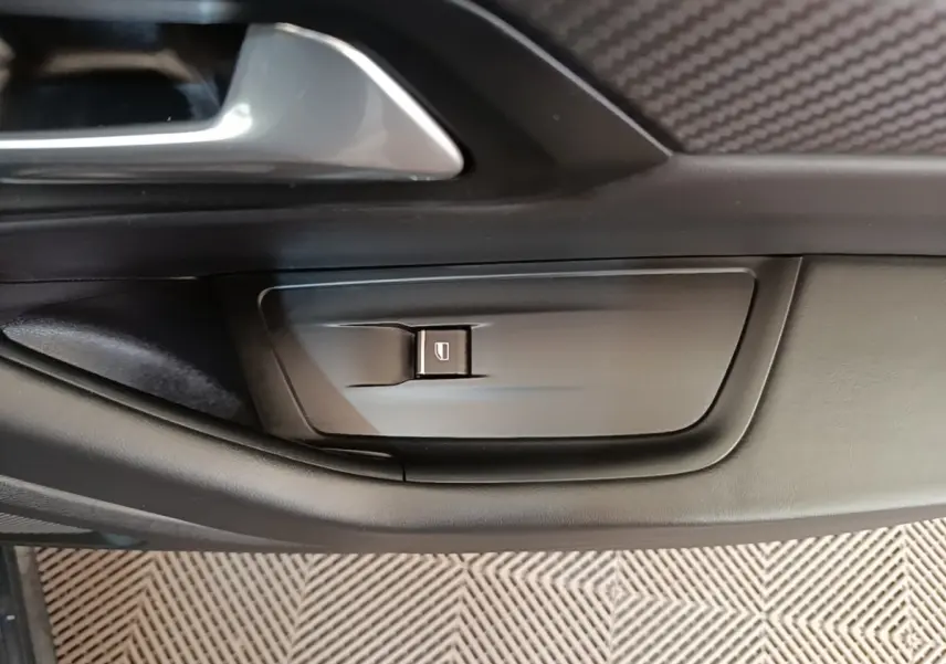 Détail de la commande de lève-vitre côté conducteur sur la porte intérieure noire d'une Peugeot 508 gris foncé.