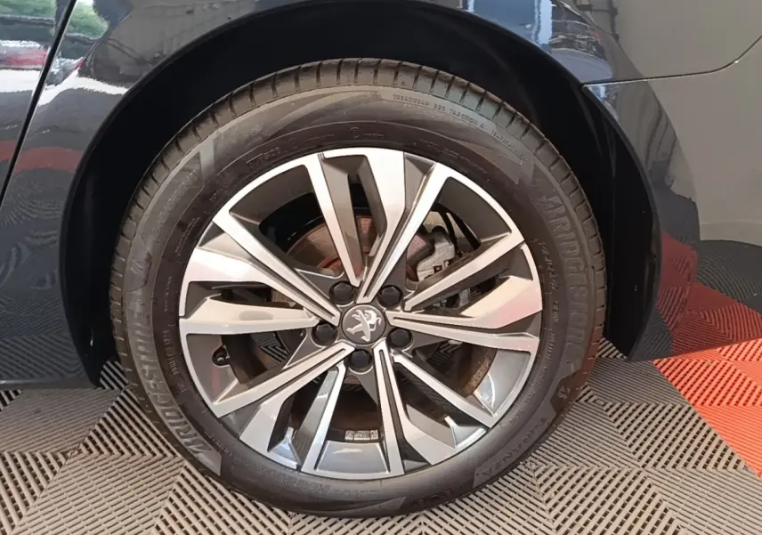 Gros plan sur la roue avant droite d’une Peugeot 508 gris foncé avec jante alliage au design moderne.