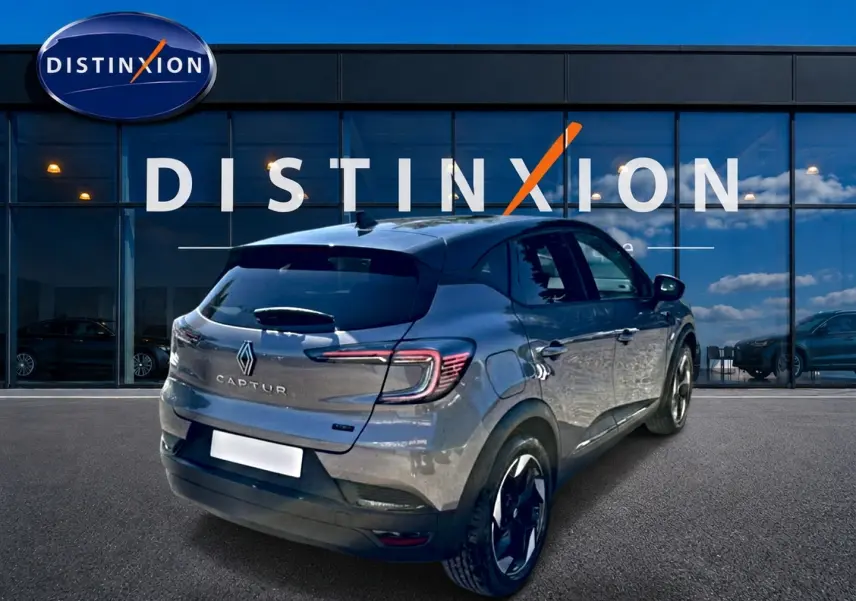 Vue 3/4 arrière droite d'un Renault Captur gris cassiopée 2026 devant une vitrine Distinxion, jantes noires et feux LED.