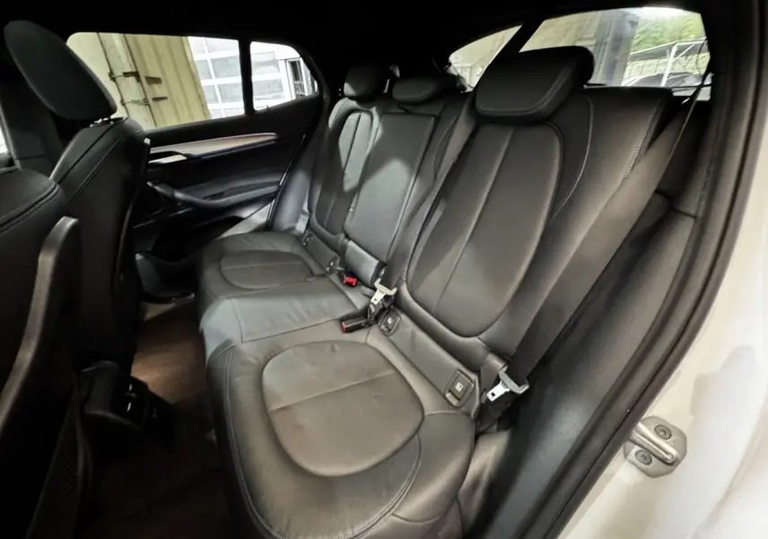 Vue intérieure côté droit montrant la banquette arrière en cuir noir d'une BMW X2 blanche, avec ceinture de sécurité visible.