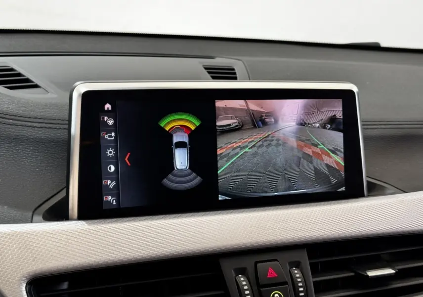 Écran central du BMW X2 blanc montrant la caméra de recul et l’alerte de proximité en stationnement.