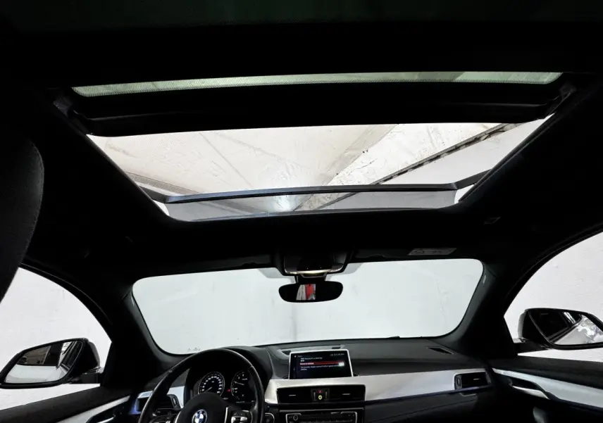 Vue intérieure avant du BMW X2 blanc xDrive25e M Sport 2022, avec toit panoramique et tableau de bord moderne.