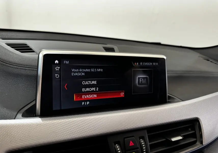Écran central tactile du tableau de bord du BMW X2 blanc, affichant la radio FM sur la station Evasion.