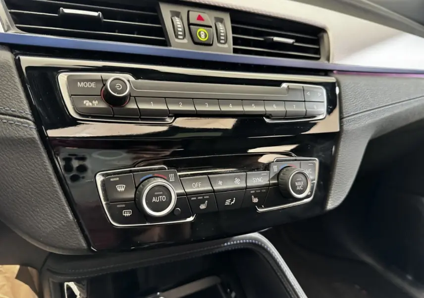 Gros plan sur la console centrale noire brillante du BMW X2 xDrive25e M Sport 2022, avec commandes climatisation et multimédia.
