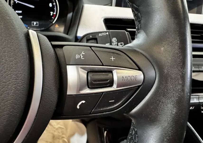 Gros plan sur les commandes multifonctions en cuir et aluminium du volant du BMW X2 xDrive25e blanc de 2022.