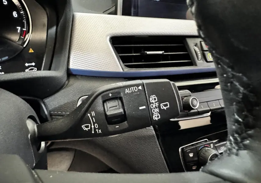 Gros plan sur la commande d’essuie-glace à gauche du volant dans l’habitacle noir et gris du BMW X2 blanc.