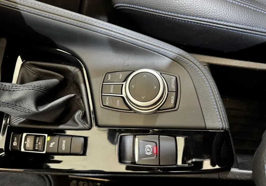 Gros plan sur la console centrale noire du BMW X2 blanc, avec molette de navigation et levier de vitesse cuir.