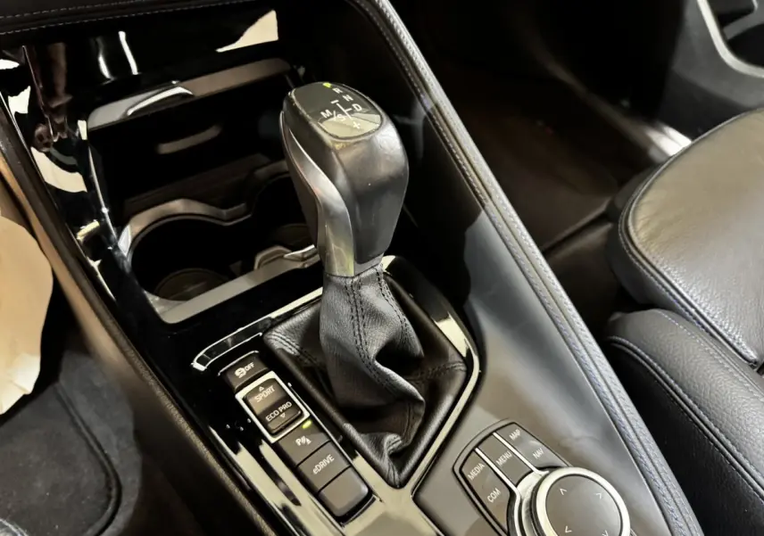 Gros plan sur la console centrale noire du BMW X2 blanc, mettant en valeur le levier de vitesse et les commandes multimédia.