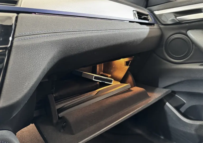 Intérieur BMW X2 xDrive25e 2022, vue côté passager sur boîte à gants ouverte avec éclairage intérieur.