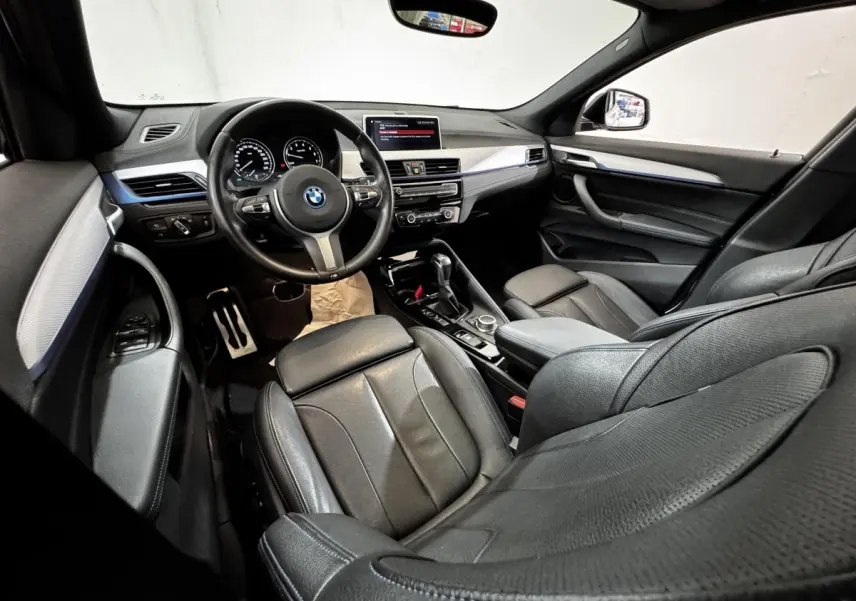 Intérieur noir de BMW X2 xDrive25e 2022 vu côté conducteur, avec tableau de bord moderne et volant multifonction.