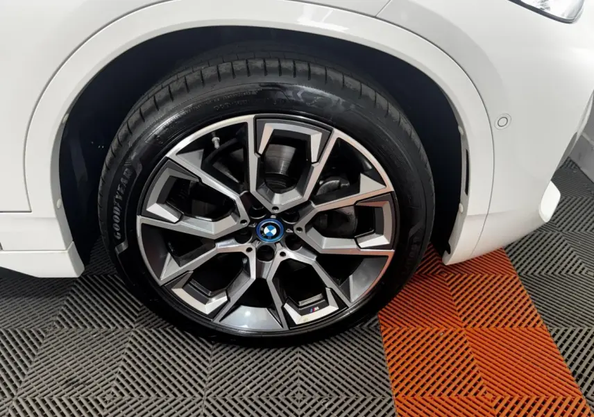Gros plan sur la roue avant droite d’un BMW X2 blanc, jante alliage M sport avec logo coloré au centre.