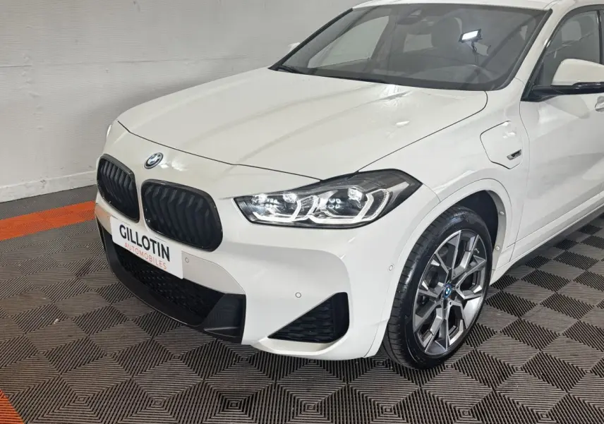 BMW X2 xDrive25e blanc vue 3/4 avant droit, calandre noire et jantes alliage distinctives.