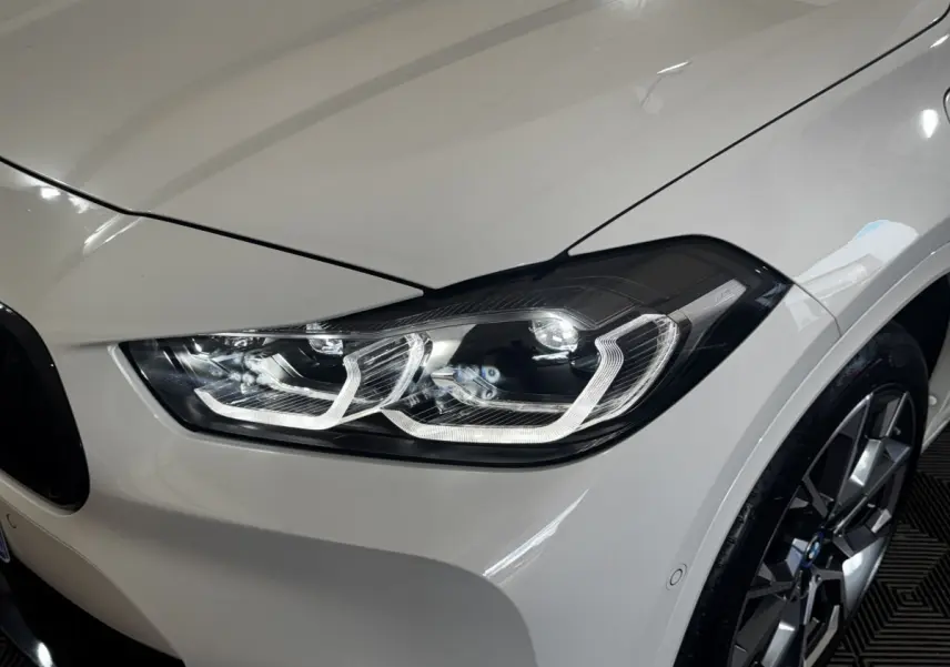 Gros plan sur le phare avant droit blanc d'un BMW X2 xDrive25e M Sport 2022 avec jante alliage visible.