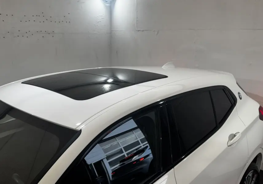 Vue 3/4 arrière droite d’un BMW X2 blanc avec toit panoramique noir et vitres teintées dans un garage.