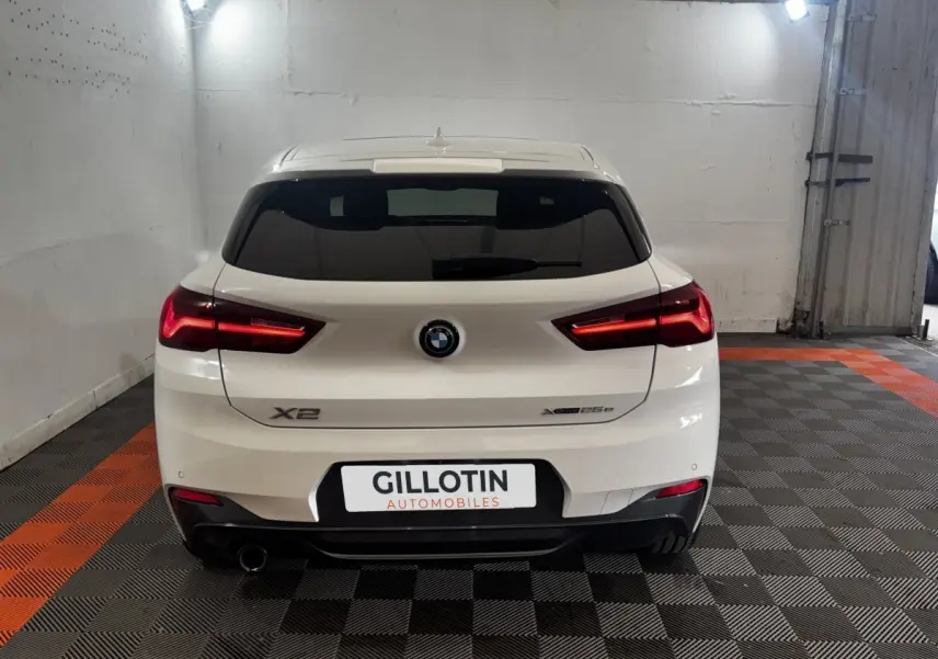 Vue arrière d'un BMW X2 blanc xDrive25e M Sport 2022 avec feux LED allumés dans un garage.