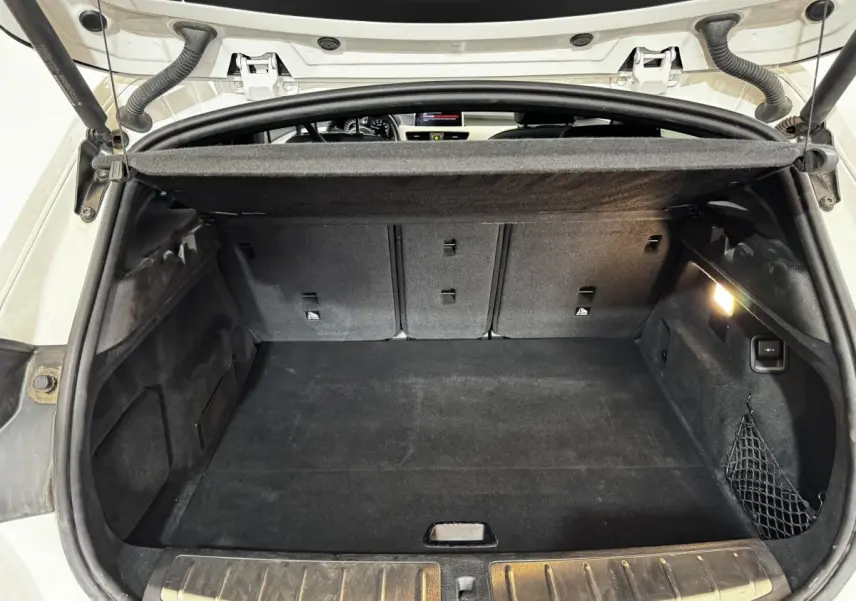 Coffre ouvert d’un BMW X2 blanc, vue intérieure montrant la banquette arrière rabattable et la protection aluminium des seuils.